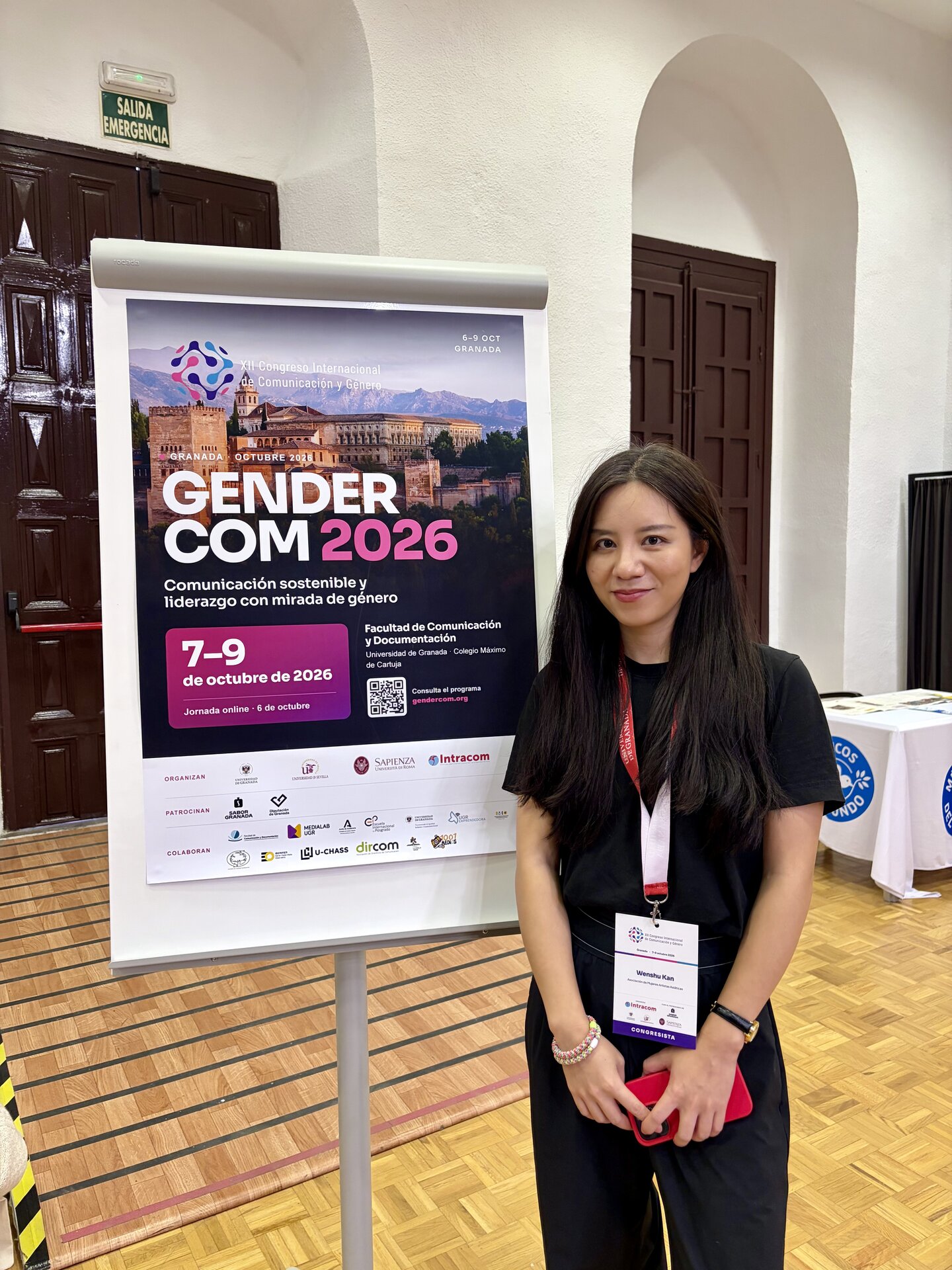 Wenshu Kan, fundadora de AMASIA, junto al cartel de GENDERCOM 2026